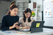 © Wasana - Two women are sitting at a desk with a laptop and a cell phone