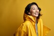 © CogniLens - Portrait of a joyful asian woman in her 40s wearing a vibrant raincoat isolated in soft brown background