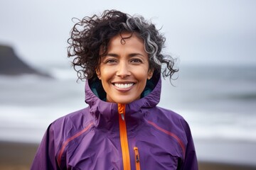Wall Mural - Portrait of a happy indian woman in her 50s wearing a functional windbreaker on crashing waves background
