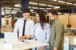 © Studio Romantic - Young caucasian couple standing at building market or big shopping mall with male friendly salesman manager helping them to make purchase in hypermarket. Man seller consulting customers