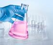 © volff - Conical flask in hand in blue glove and laboratory equipment at the background.