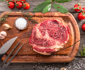 Canvas Print - Raw beef steaks with herbs and spices ready for cooking are on wooden board.