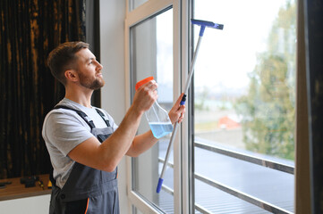 Male professional cleaning service worker in overalls cleans the windows and shop windows of a store with special equipment