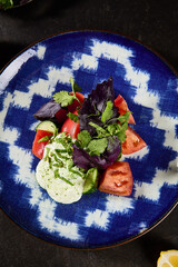 Wall Mural - Refreshing Eastern Salad with Tomatoes, Basil, and Sour Cream on a Blue Porcelain Plate