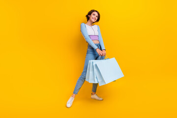 Wall Mural - Full body portrait of creative lovely lady hold store bags look empty space isolated on yellow color background