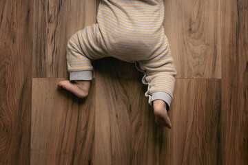 Closeup of barefoot baby feet on a wooden floor at home, view from above