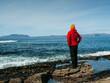 © mark_gusev - A man in a red jacket stands on a rock overlooking the ocean. The man is wearing a yellow hat and he is looking out at the water. The scene is peaceful and serene. West coast of Ireland. Travel theme