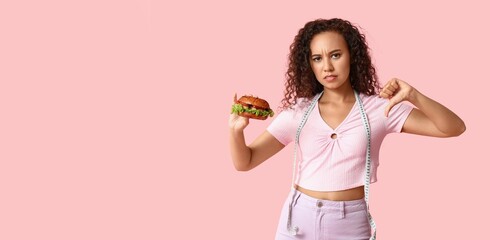 Canvas Print - Sad African-American woman with measuring tape and burger showing thumb-down on pink background with space for text. Diet concept