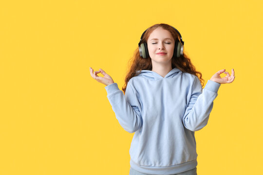 Portrait of relaxed young woman meditating while listening to music on yellow background