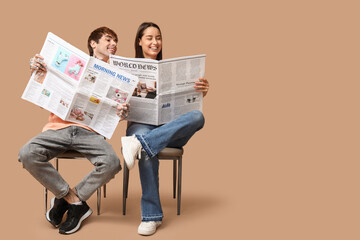 Canvas Print - Young couple with newspapers on beige background