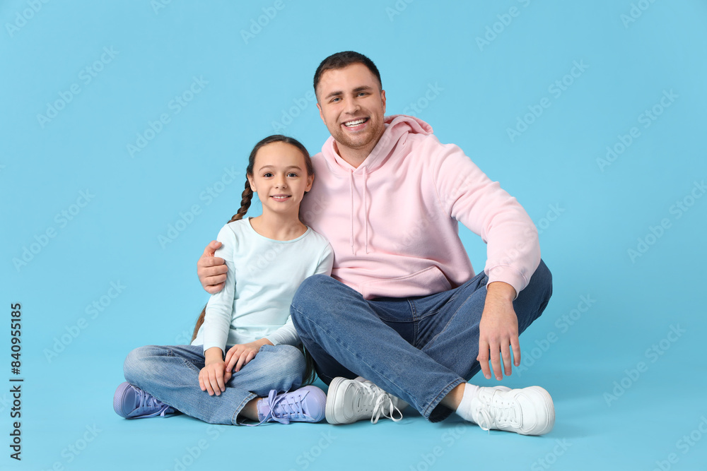 Father and his daughter sitting on blue background