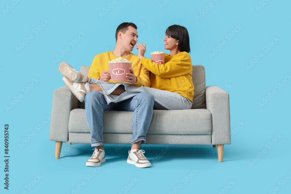 Young couple in love eating popcorn on sofa against blue background
