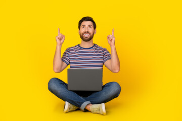 Photo of young modern guy with laptop using gadget directing fingers above copyspace website isolated on yellow color background