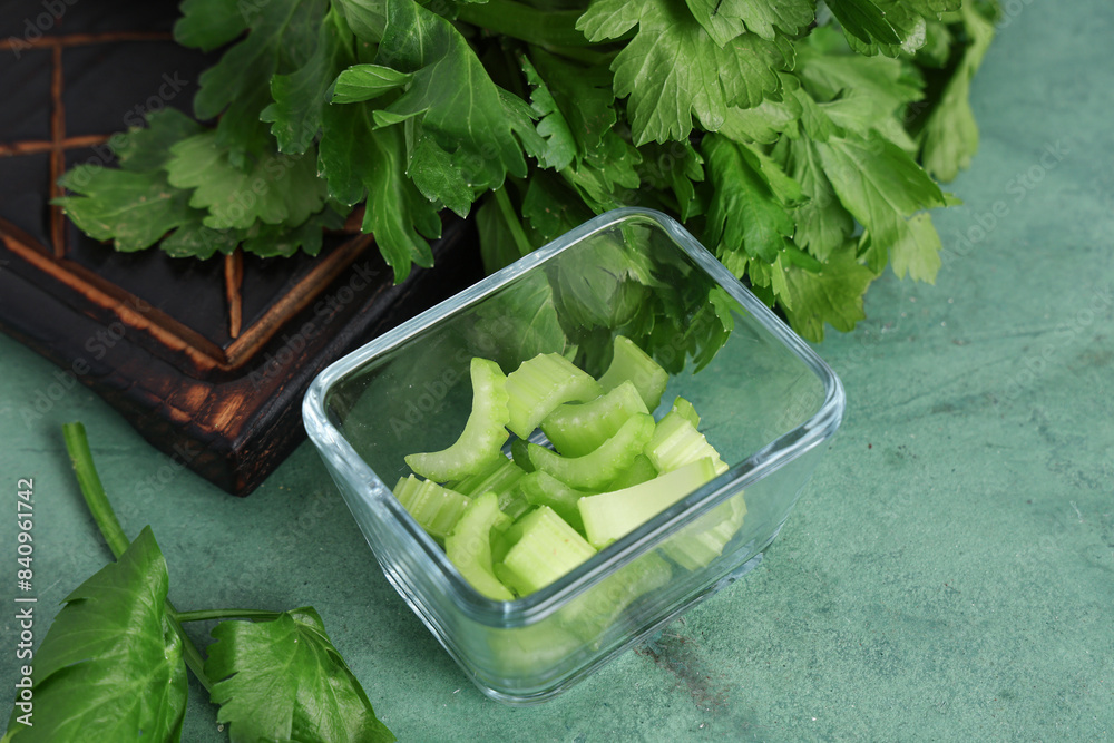 Board and glass bowl with fresh green celery on color background