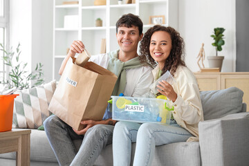 Wall Mural - Young couple sorting rubbish on sofa at home