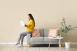 © Pixel-Shot - Young Asian woman using laptop on grey sofa near beige wall