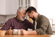 © New Africa - Happy son and his dad with cups at wooden table in kitchen