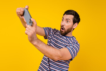 Poster - Photo of impressed man with beard dressed striped t-shirt look at smartphone play video game isolated on vibrant yellow color background