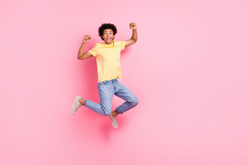 Wall Mural - Full length portrait of nice young man jump raise fists empty space wear yellow t-shirt isolated on pink color background