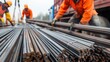 © Khoirul - Unloading iron pipes and rebar from the top of a truck by workers at a construction site.