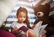 © Lyndon/peopleimages.com - Learning, kid and reading book in home tent for education, language development or knowledge in bedroom. Girl child, fairytale or studying fantasy story, information or hobby with teddy bear in house