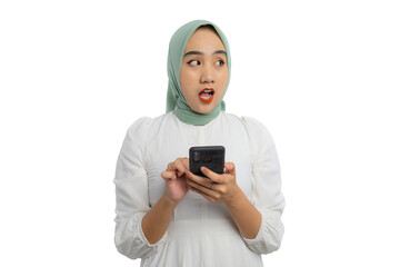 Wall Mural - Shocked young Asian woman in green hijab and white blouse holding smartphone and looking aside at copy space, showing amazed expression isolated on white background