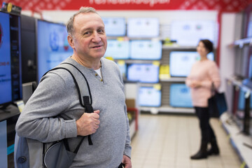 Wall Mural - European mature man standing in televisions department in appliance store and looking at camera.