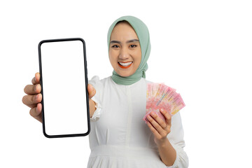 Wall Mural - Happy young Asian woman in green hijab and white blouse holding mobile phone with blank screen and money isolated on white background