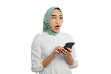 Wall Mural - Shocked young Asian woman in green hijab and white blouse holding smartphone and looking aside at copy space, showing amazed expression isolated on white background