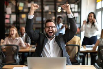 Poster - A man is sitting at a desk with a computer and a laptop. He is smiling and he is celebrating something