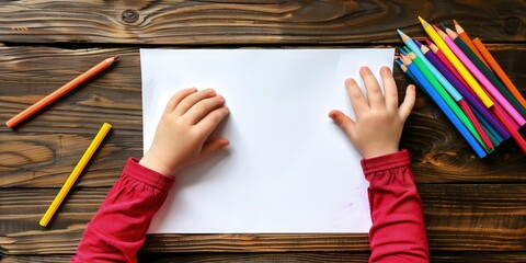 A blank white paper on the table with child hands. a child is coloring, the child has crayons in her hands.