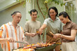 © DragonImages - Friends checking if meat and veggies kebabs are cooked