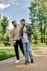 A bearded gay couple walks hand-in-hand through a lush green park, laughing and enjoying each others company.