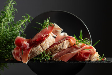 Wall Mural - Ciabatta with prosciutto and rosemary on a black background.