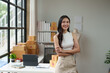 © Phimwilai - Independent business woman Asian freelance female employee smiling brightly Standing with arms crossed confidently, happy standing in the office, working online. Parcel shipping.