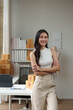 © Phimwilai - Independent business woman Asian freelance female employee smiling brightly Standing with arms crossed confidently, happy standing in the office, working online. Parcel shipping.