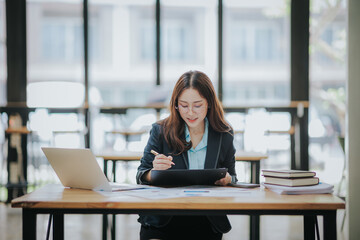 Wall Mural - Young Asian professional business woman office worker analyst sitting at desk working on laptop thinking on project plan, analyzing marketing or financial data online, watching elearning webinar.