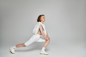 Wall Mural - Mature woman in comfortable attire performing a squat on a white background.