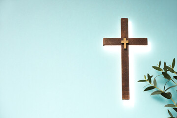 Wall Mural - Shining cross and eucalyptus branches on turquoise background, space for text. Religion of Christianity