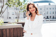 © halayalex - Young beautiful brunette woman wearing nice trendy white suit jacket. Sexy smiling model posing in the street. Fashionable female using mobile phone. Makes call, chatting. Talks, speaks at smartphone