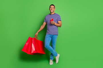 Sticker - Photo of positive nice guy wear striped stylish denim clothes hold packages isolated on green color background