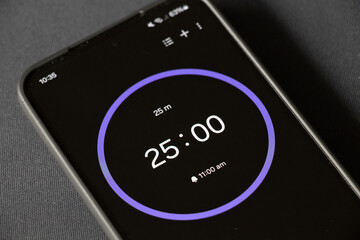 A phone with a black and white 25-minute timer to study with the pomodoro method on a blurry background. Perfect for students planning their time studying, doing homework, being productive.