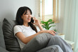 © Prathankarnpap - Smiling young woman in casual clothes having g pleasant phone conversation in living room