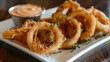 © Plaifah - A platter of golden and crispy onion rings served with a side of tangy dipping sauce, a popular appetizer choice at casual dining restaurants and fast-food chains
