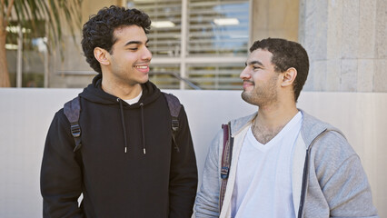 Sticker - Two smiling hispanic men enjoying friendship outdoors in a sunny urban setting, exuding casual style and camaraderie.