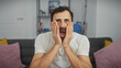 © Krakenimages.com - A surprised middle-aged man with a beard in a white shirt expressing shock in a modern living room.