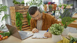 © Krakenimages.com - A young man with a beard and headphones writes intently in a flower-filled indoor environment, reflecting a creative or entrepreneurial spirit.