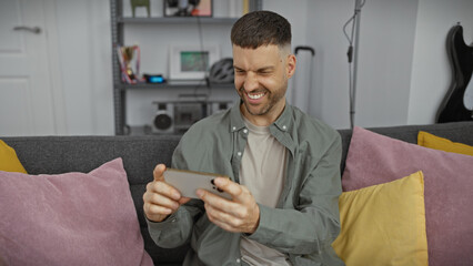 Wall Mural - Handsome man using smartphone cheerfully in cozy modern living room interior.