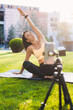 © Strelciuc - Focus in the background of woman doing stretching exercises in the park. Defocused digital smartphone in foreground recording. Blogging and vlogging. People