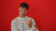 © Krakenimages.com - Handsome young hispanic man in a striped shirt posing with a thumbs-up against a vivid red background.